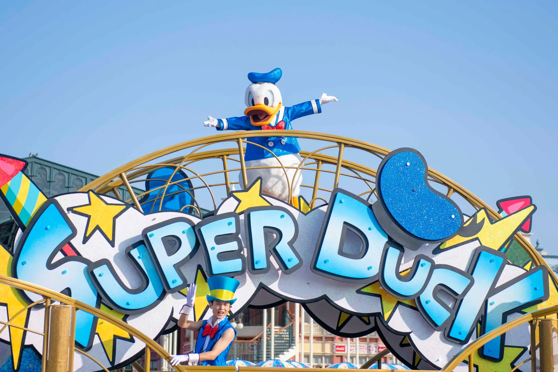 キャラクターが「SUPER DUCK」の看板上に立っている遊園地のパレードの様子。