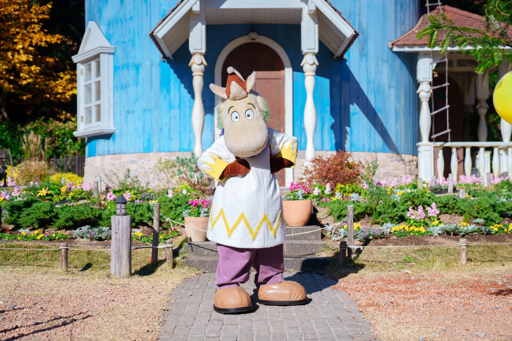 ムーミンキャラクターが青い家の前でポーズ