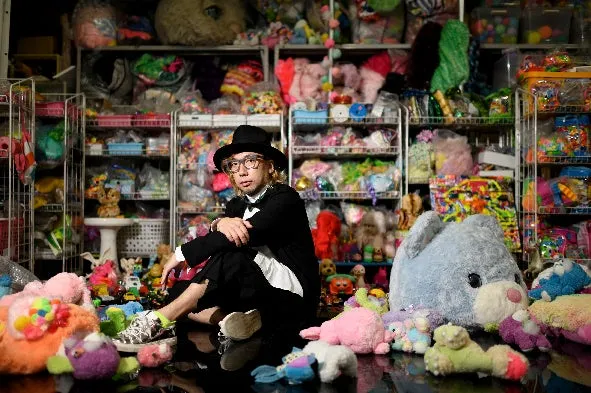 多数のカラフルなぬいぐるみに囲まれた人物