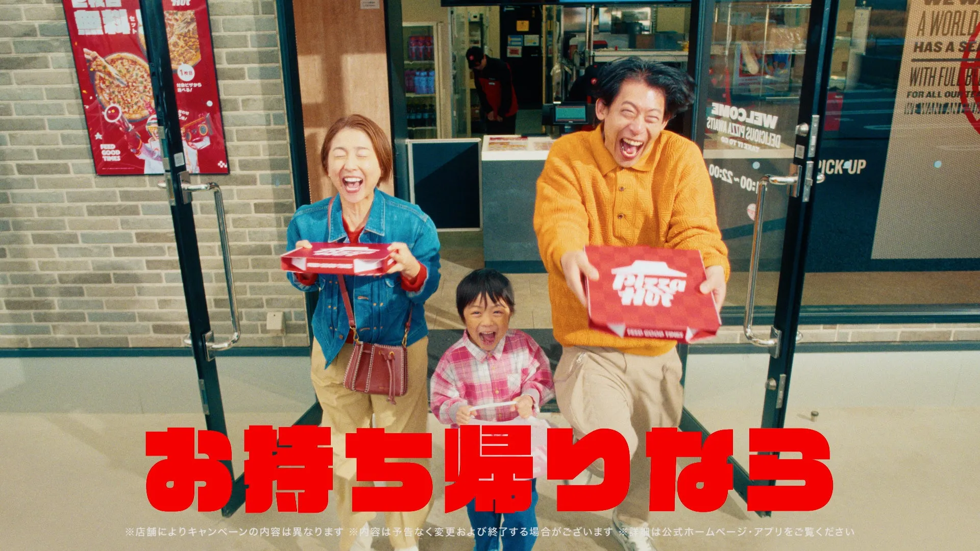 ピザショップ前でピザを持つ笑顔の家族