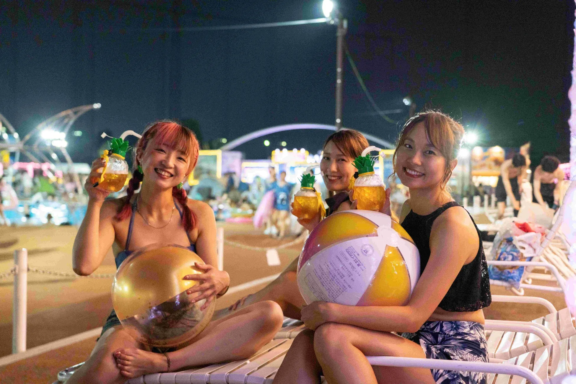 プールサイドでビーチボールとドリンクを持つ楽しげな女性たち