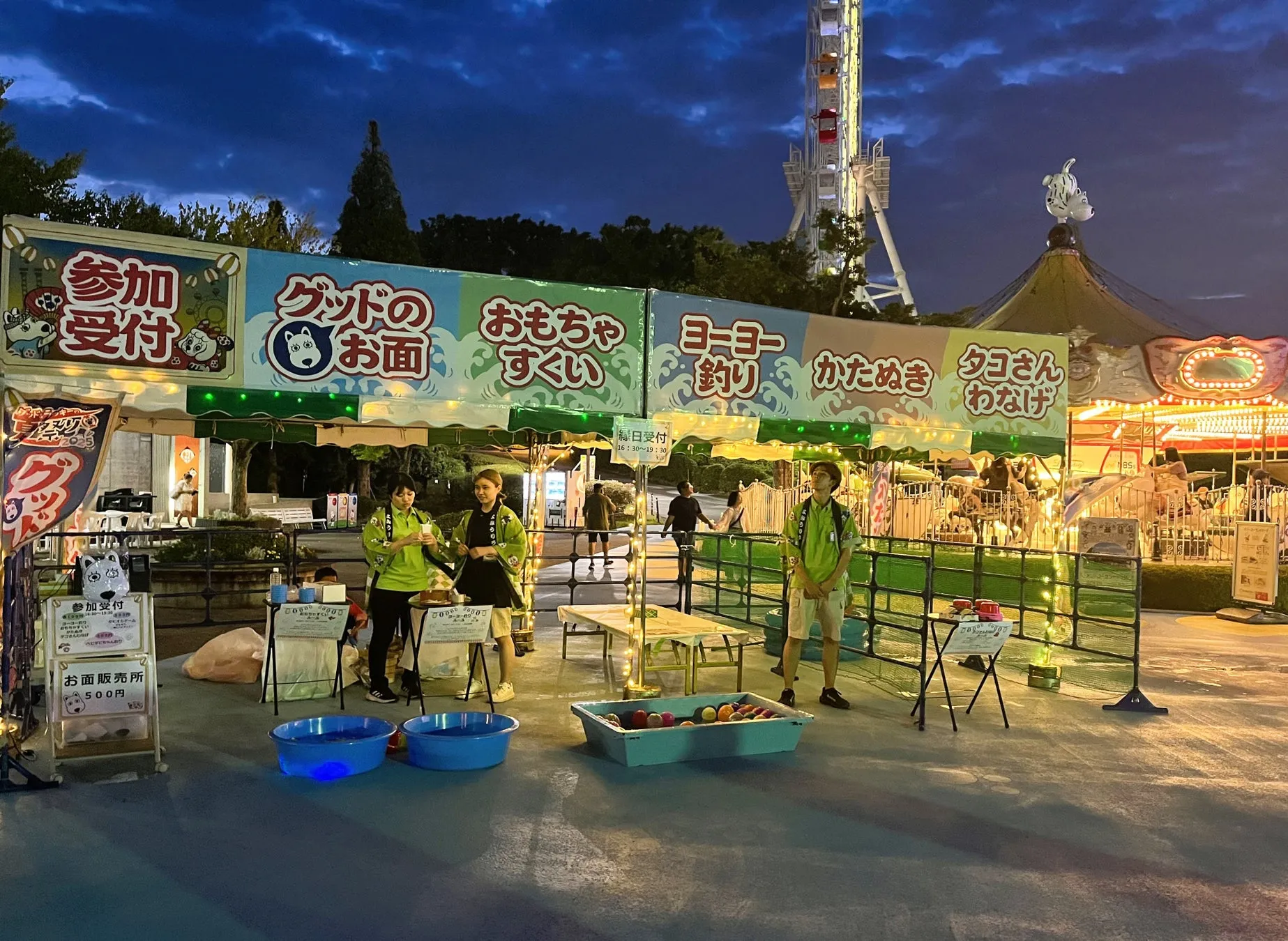 夜の遊園地の露店とスタッフ