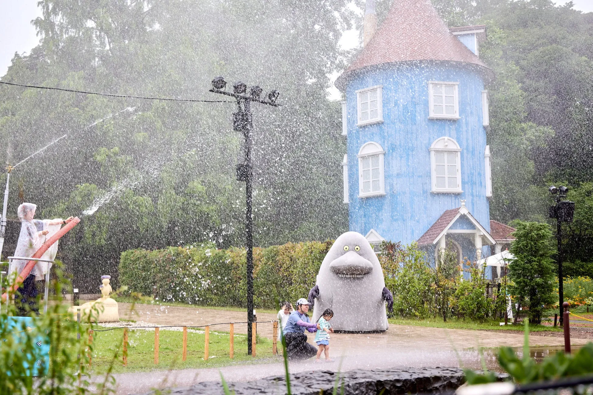 ムーミンハウス前で水遊びを楽しむ家族とキャラクター