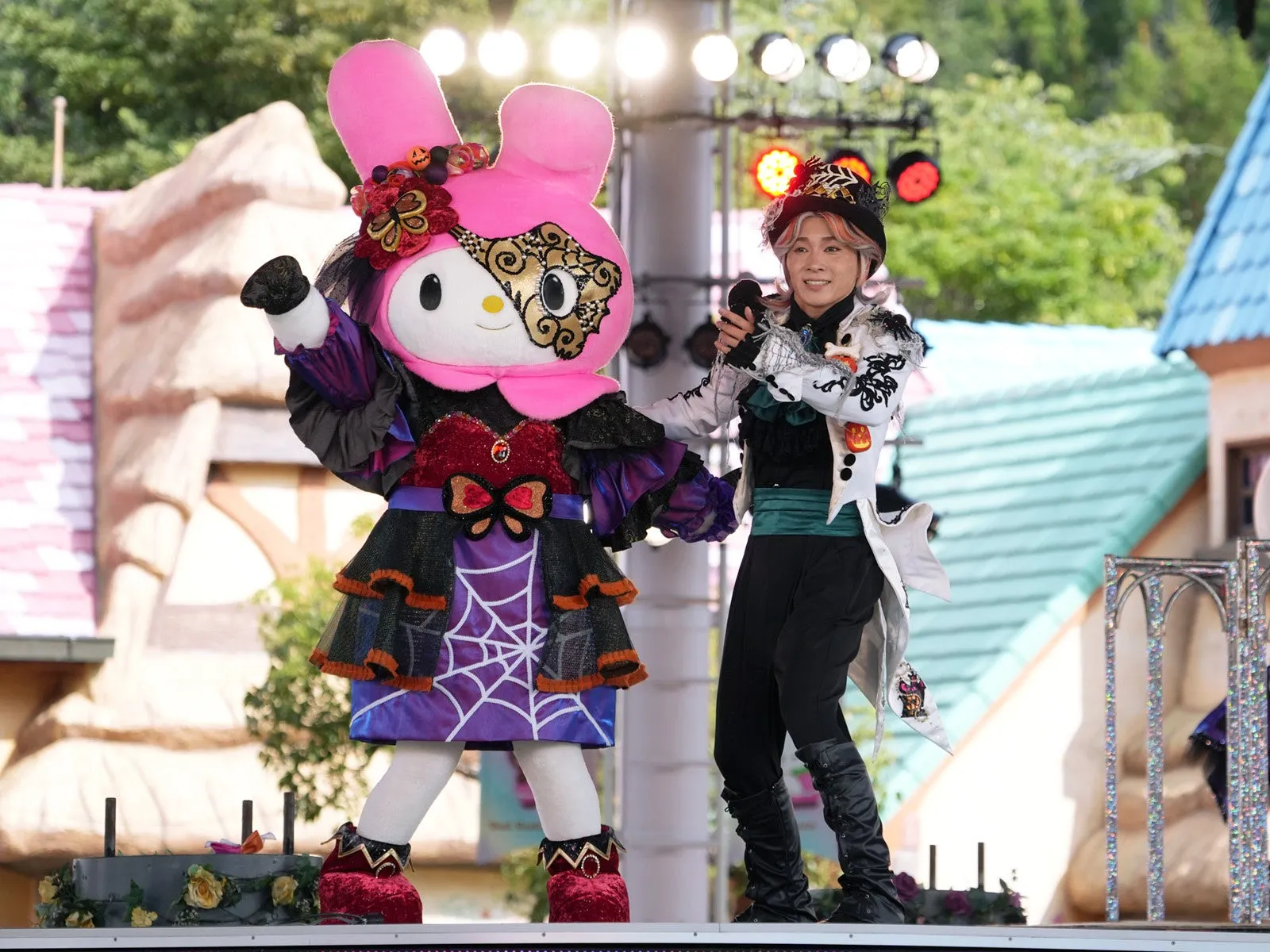 仮面をつけたキャラクターと司会者が舞台でパフォーマンス