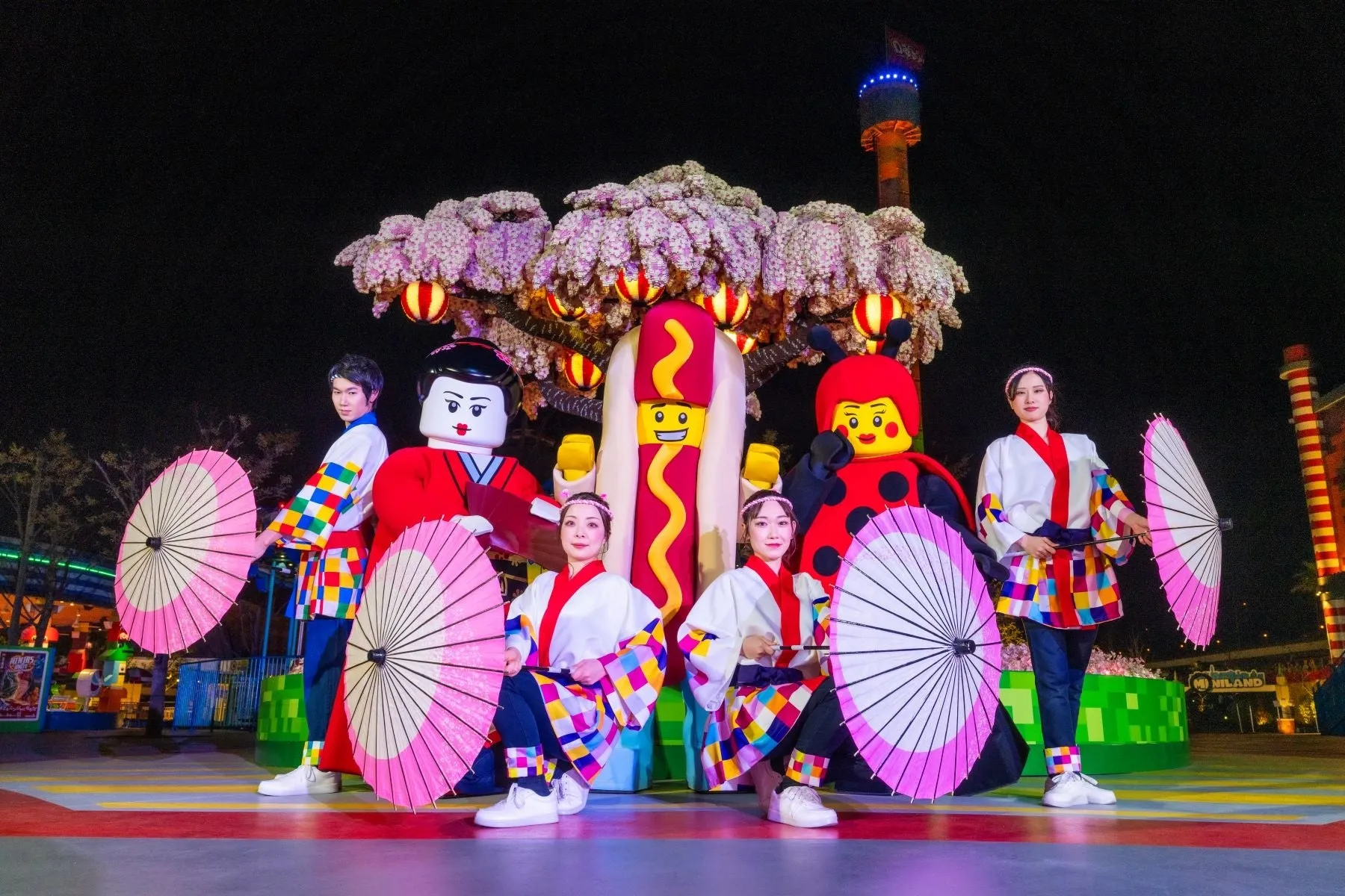 和傘を持つパフォーマーとキャラクターたちが桜の前にいる夜のイベント風景